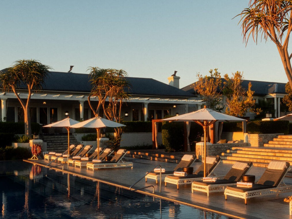 Piscina com espreguiçadeiras e guarda-sóis em frente a um lodge de estilo colonial no Shamwari, sob a luz do fim de tarde.