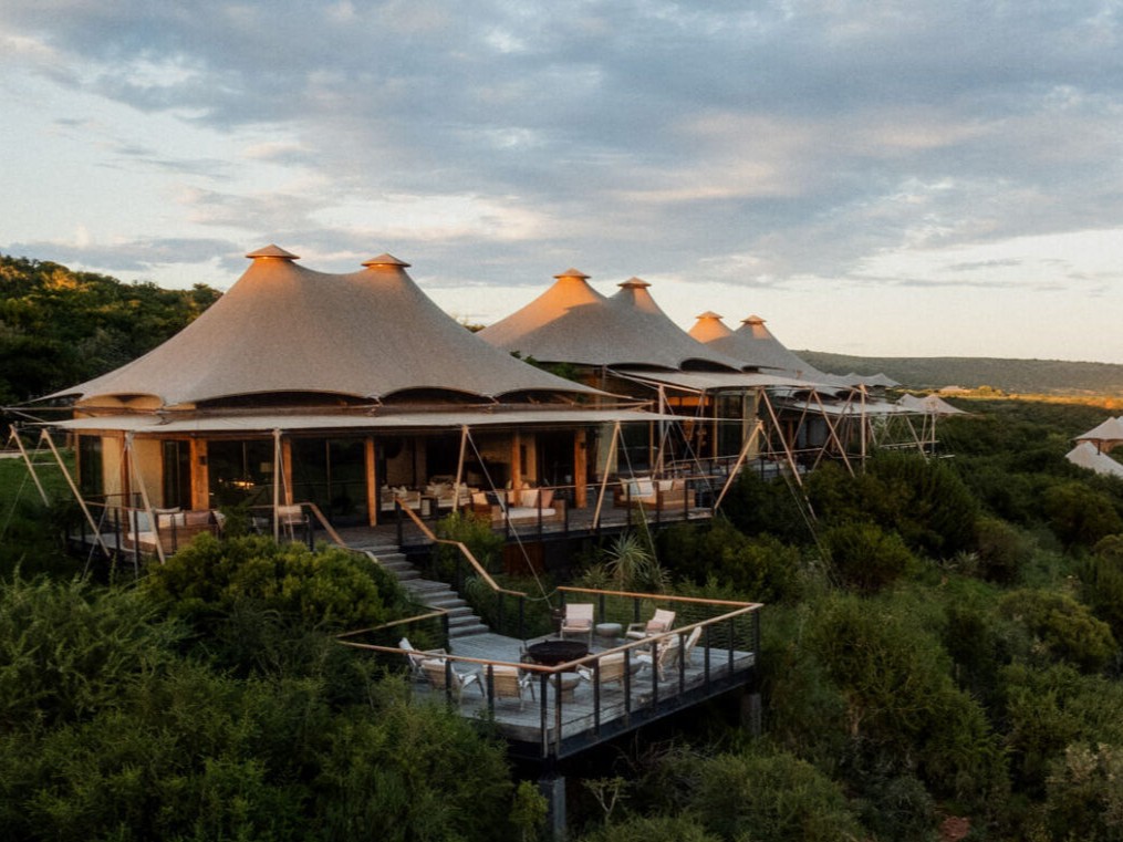 Lodge de tendas do Shamwari Private Game Reserve em uma encosta de mata, com deck e vista para a reserva ao entardecer.