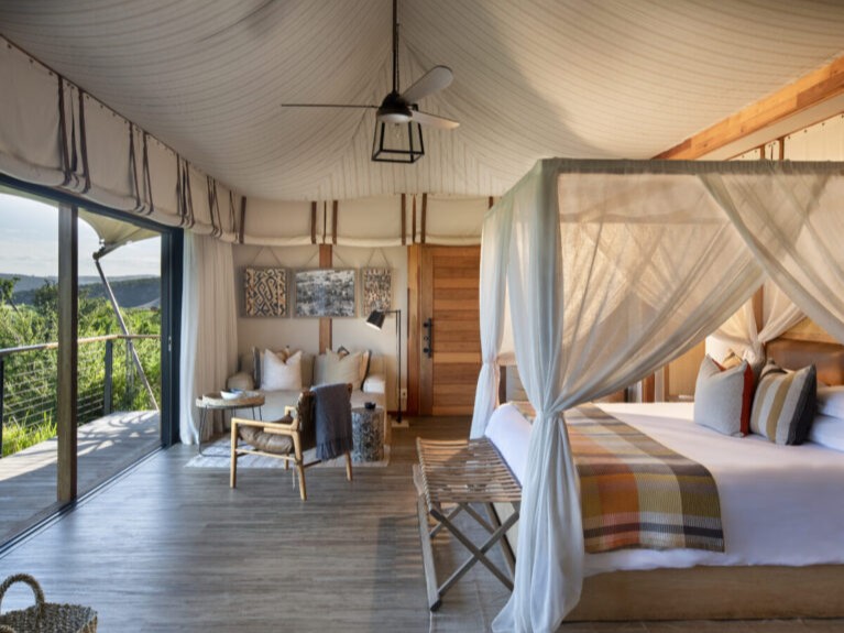 Suíte em tenda de luxo no Shamwari com cama de dossel e mosquiteiro, sala de estar e porta de vidro aberta para o deck.