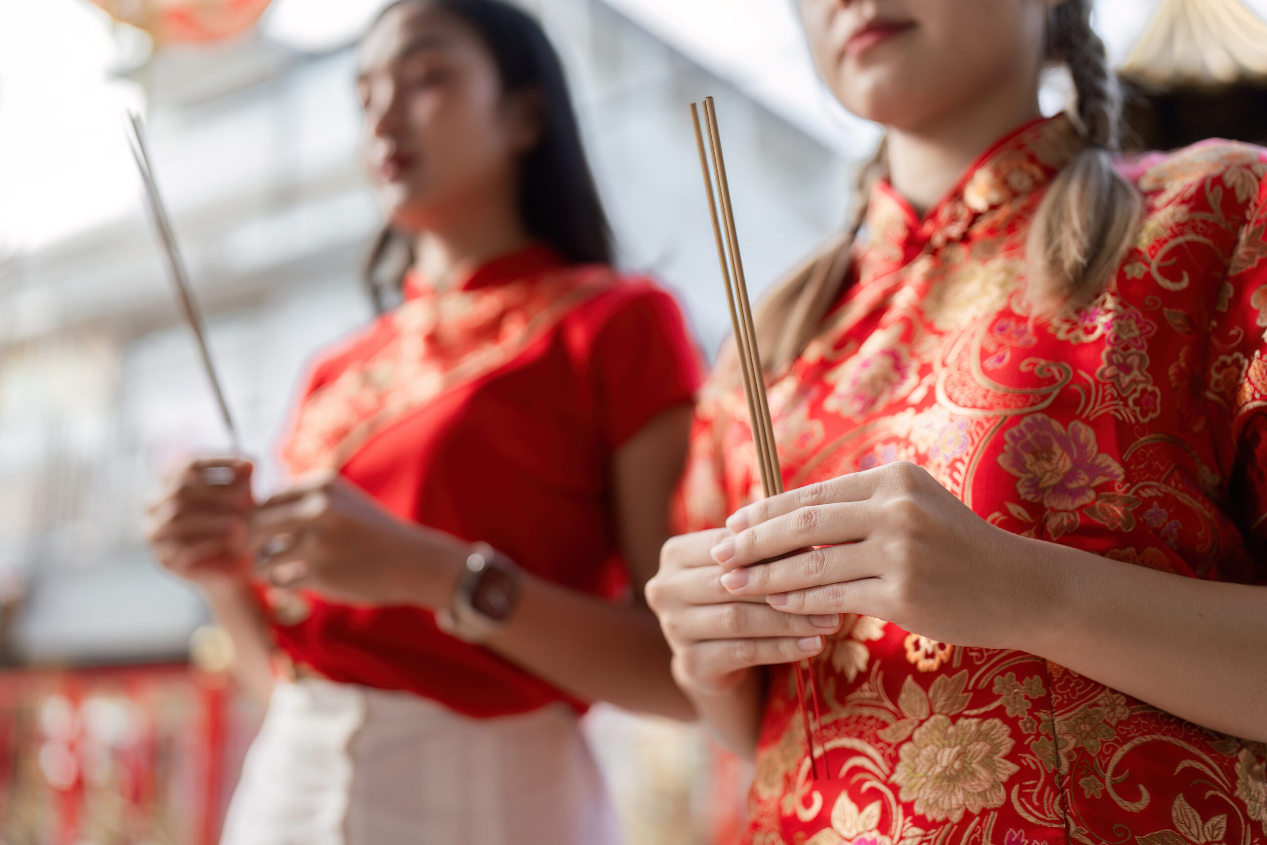 Mulheres com vestidos qipao vermelhos e dourados segurando incensos durante uma celebração tradicional chinesa.