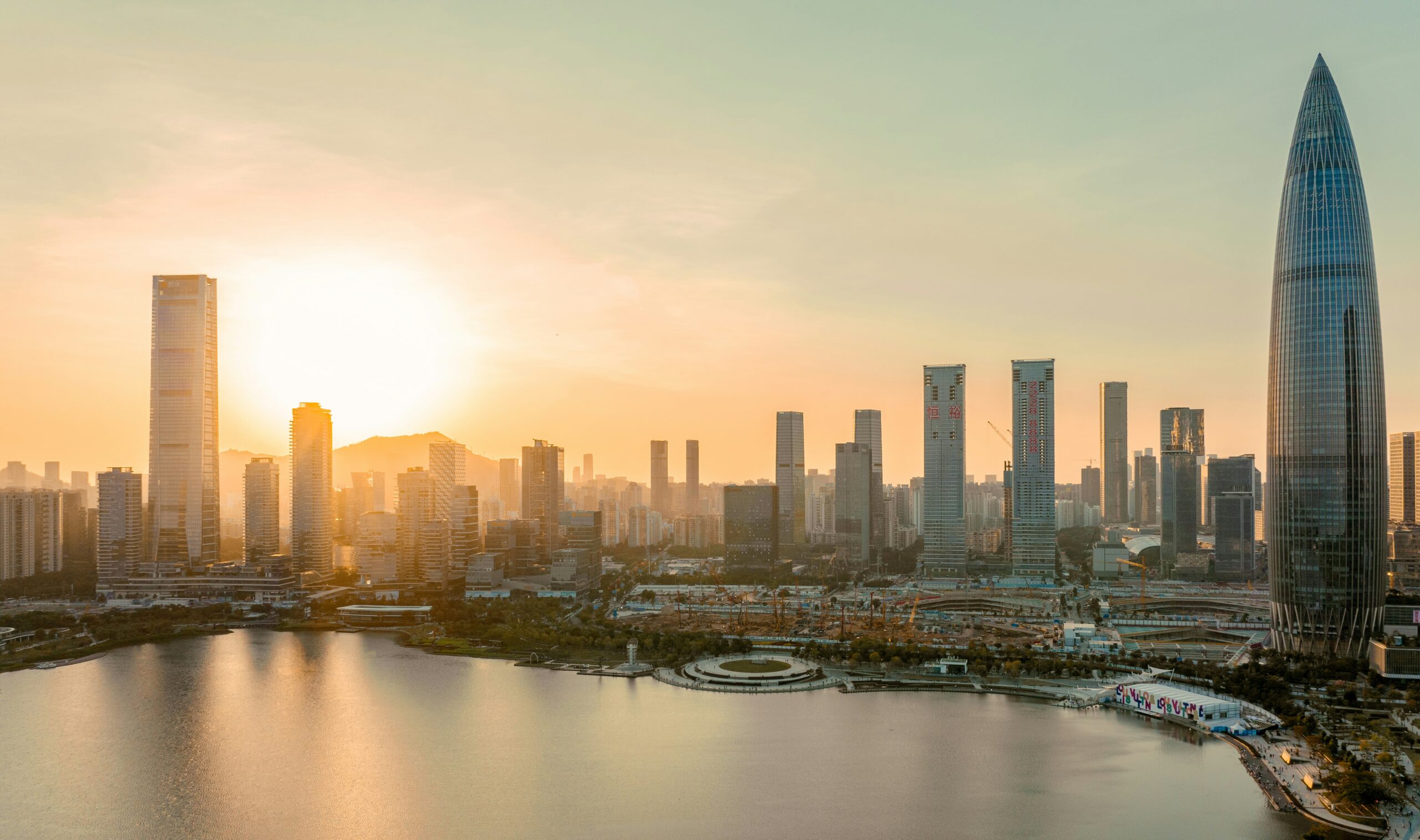 Skyline de Shenzhen ao pôr do sol, com a China Resources Tower à direita e arranha-céus refletidos na água da baía.