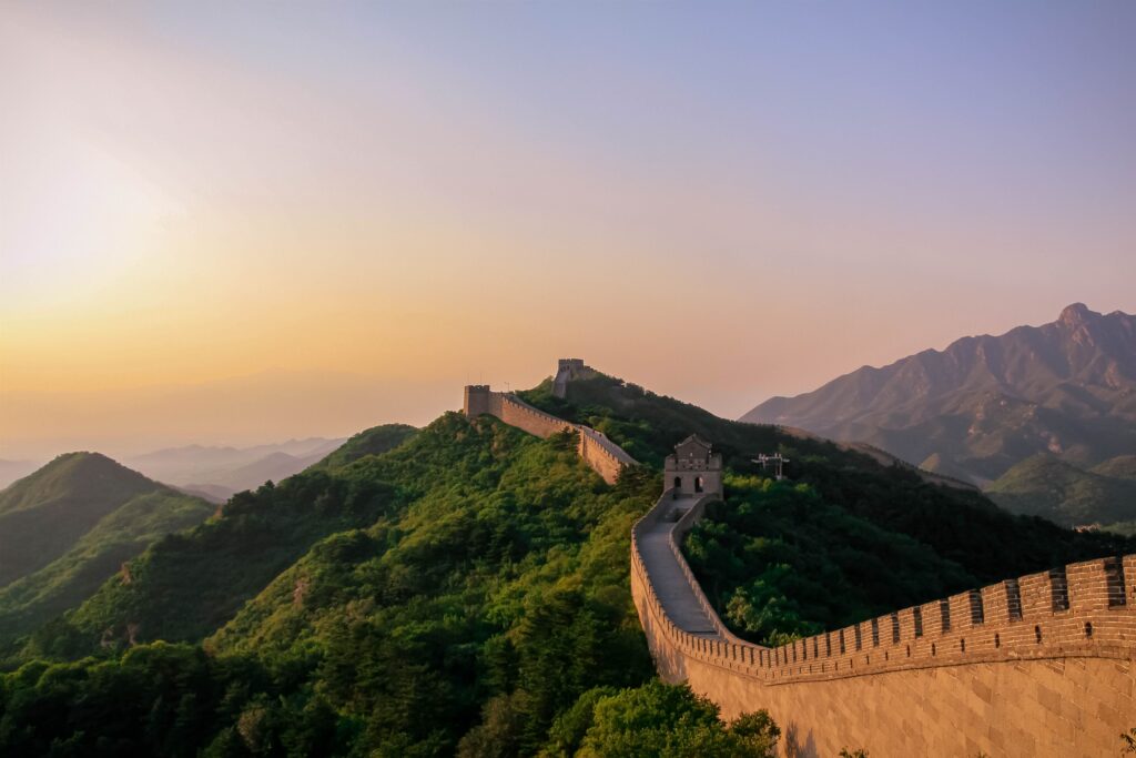 Grande Muralha da China serpenteando por montanhas verdes, com torres de vigia ao entardecer.