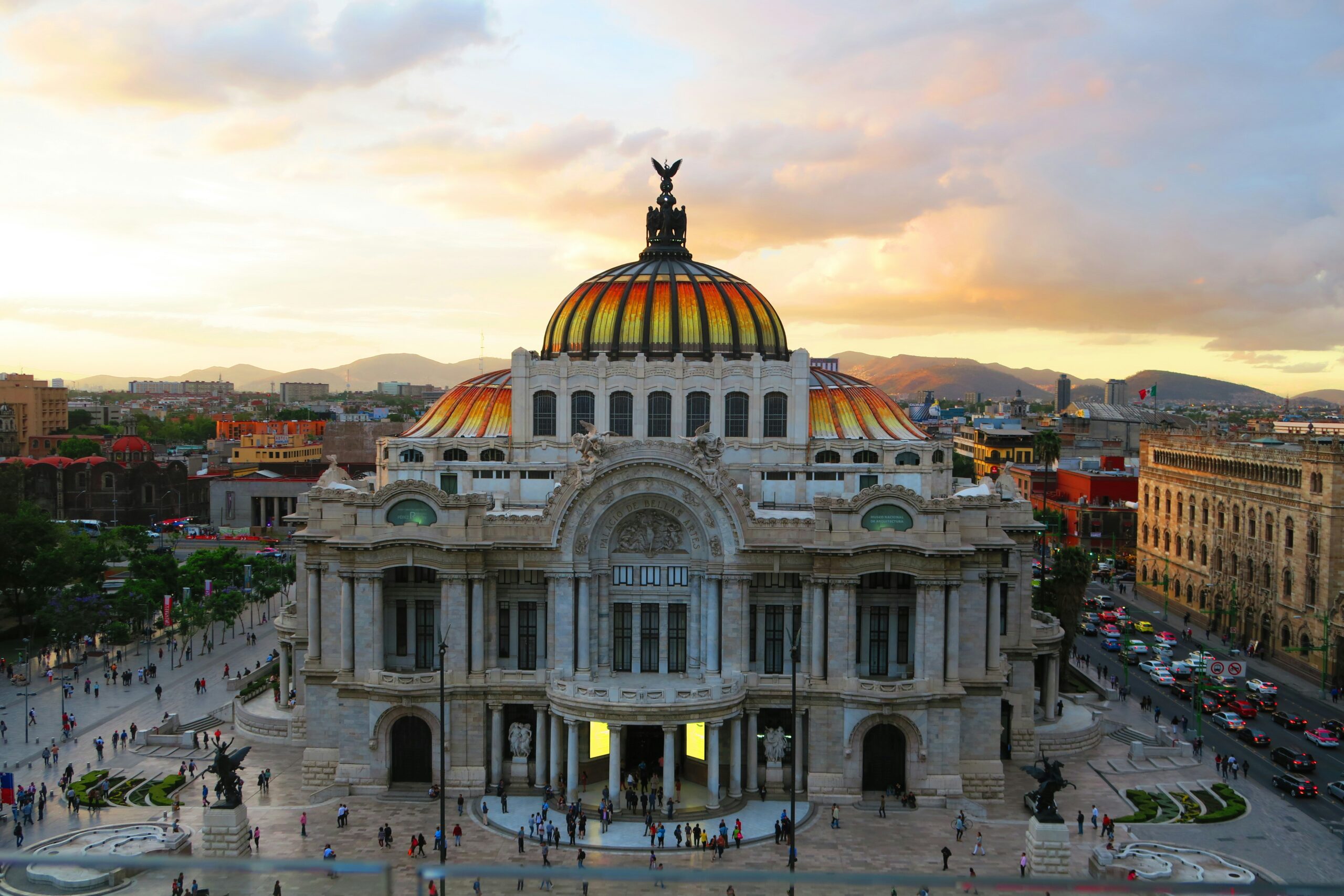 Vista aérea do Palácio de Bellas Artes na Cidade do México ao entardecer, com sua cúpula em mosaico dourado e o centro histórico ao fundo