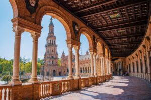 Corredor de arcos da Plaza de España em Sevilha, com a torre norte ao fundo em dia de céu azul