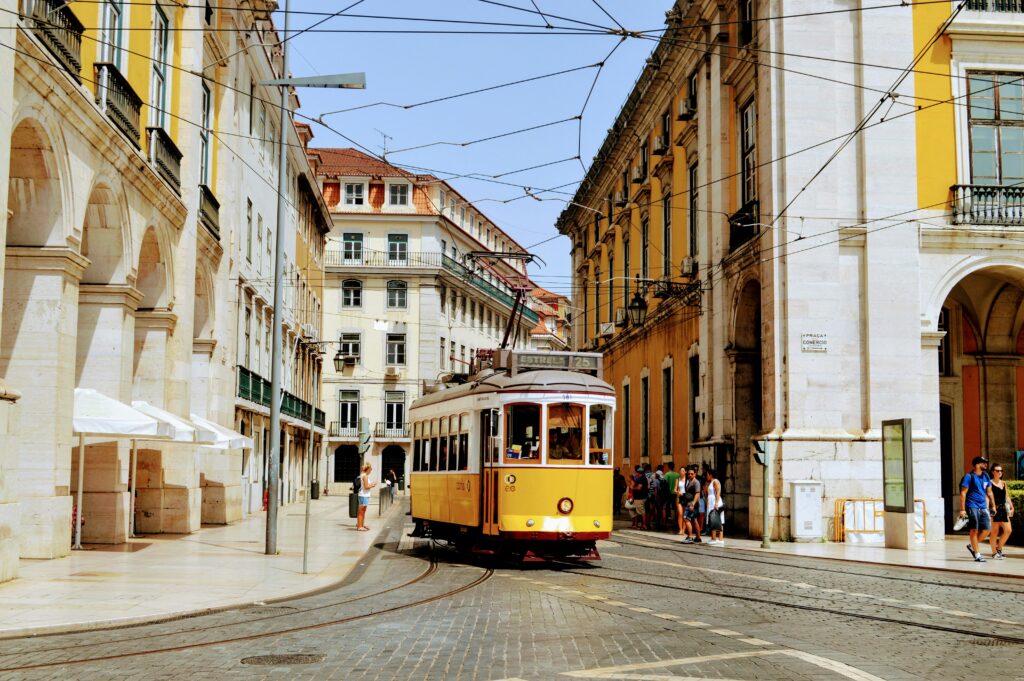 Bonde amarelo da linha 25 percorrendo as ruas de paralelepípedo da Baixa de Lisboa, com a Praça do Comércio ao fundo