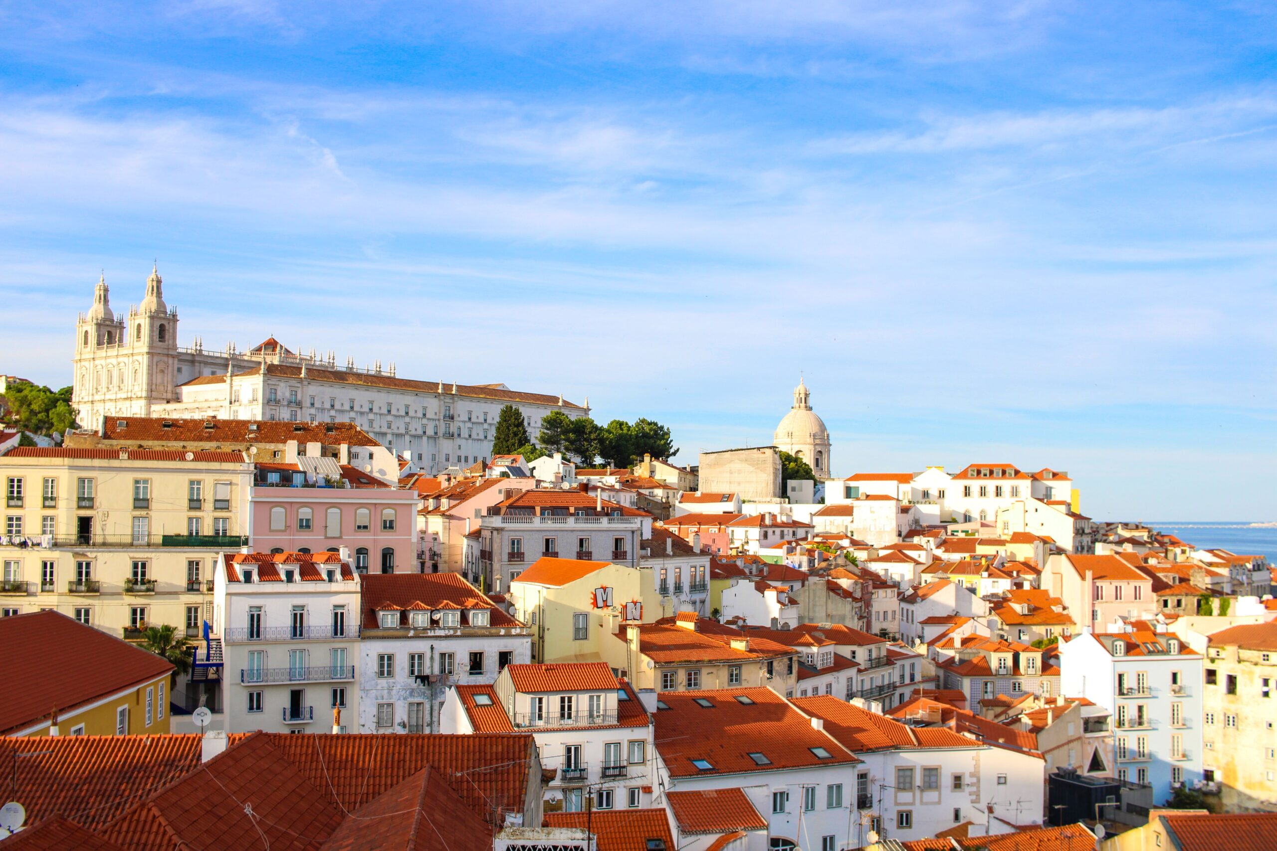Vista panorâmica do bairro da Alfama em Lisboa, com telhados de telha vermelha e o Mosteiro de São Vicente de Fora ao fundo