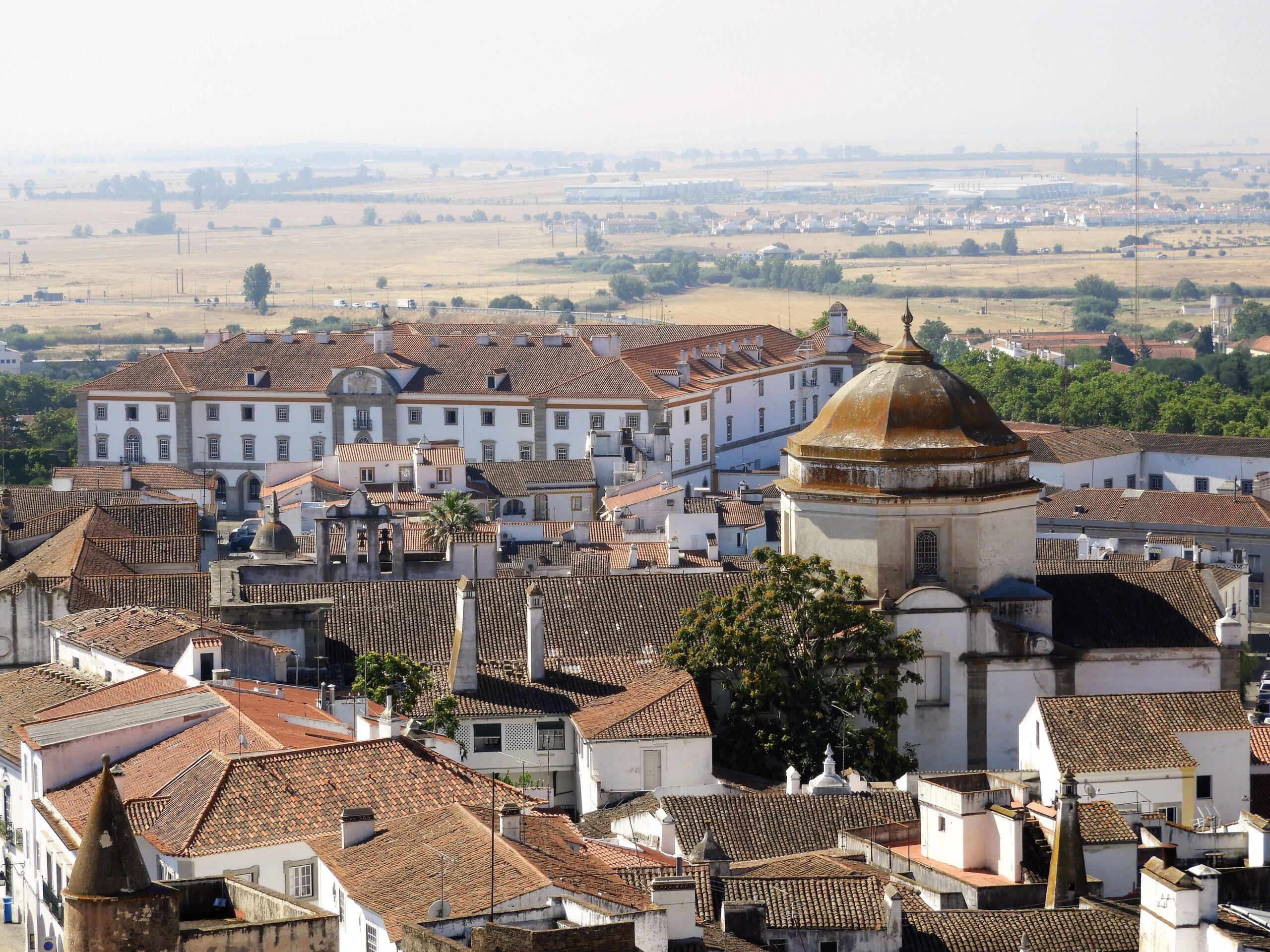 Vista panorâmica do centro histórico de Évora, no Alentejo, com casas brancas de telhado colonial e a planície alentejana ao fundo