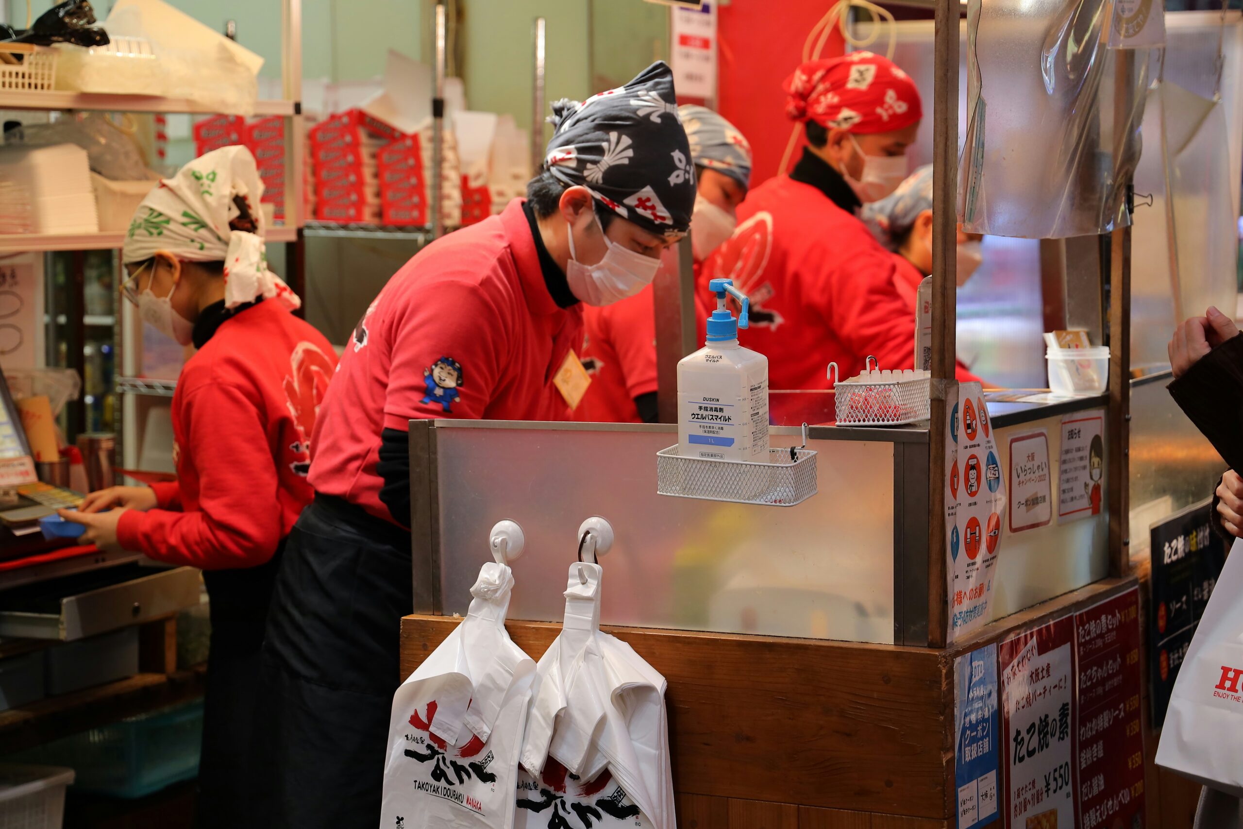 Funcionários com uniformes vermelhos preparando takoyaki em barraca de rua em Osaka, Japão