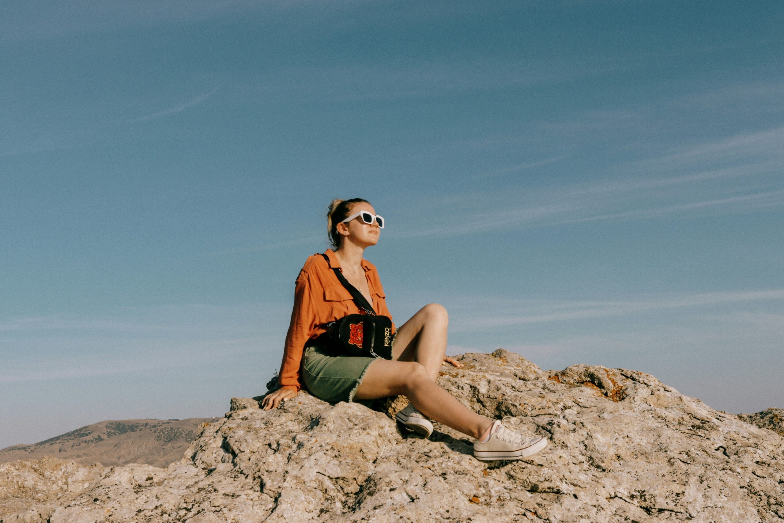 Mulher sentada no topo de uma rocha contemplando a paisagem de montanha durante viagem solo