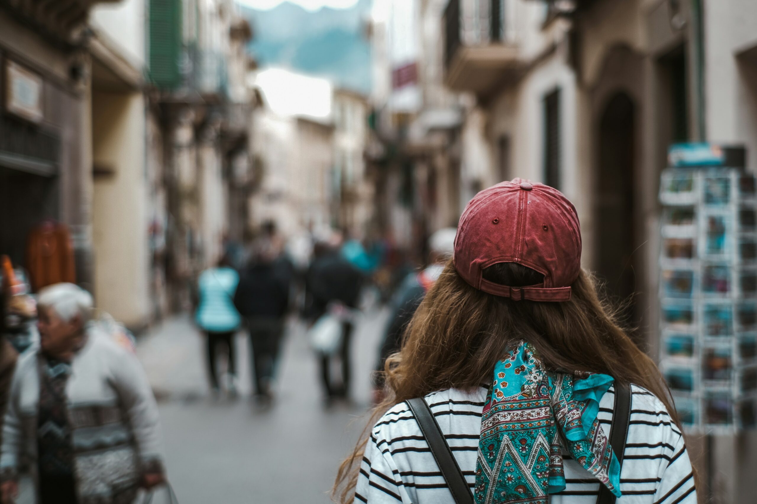 Mulher viajando sozinha caminhando por rua movimentada de cidade europeia com lojas e arquitetura histórica