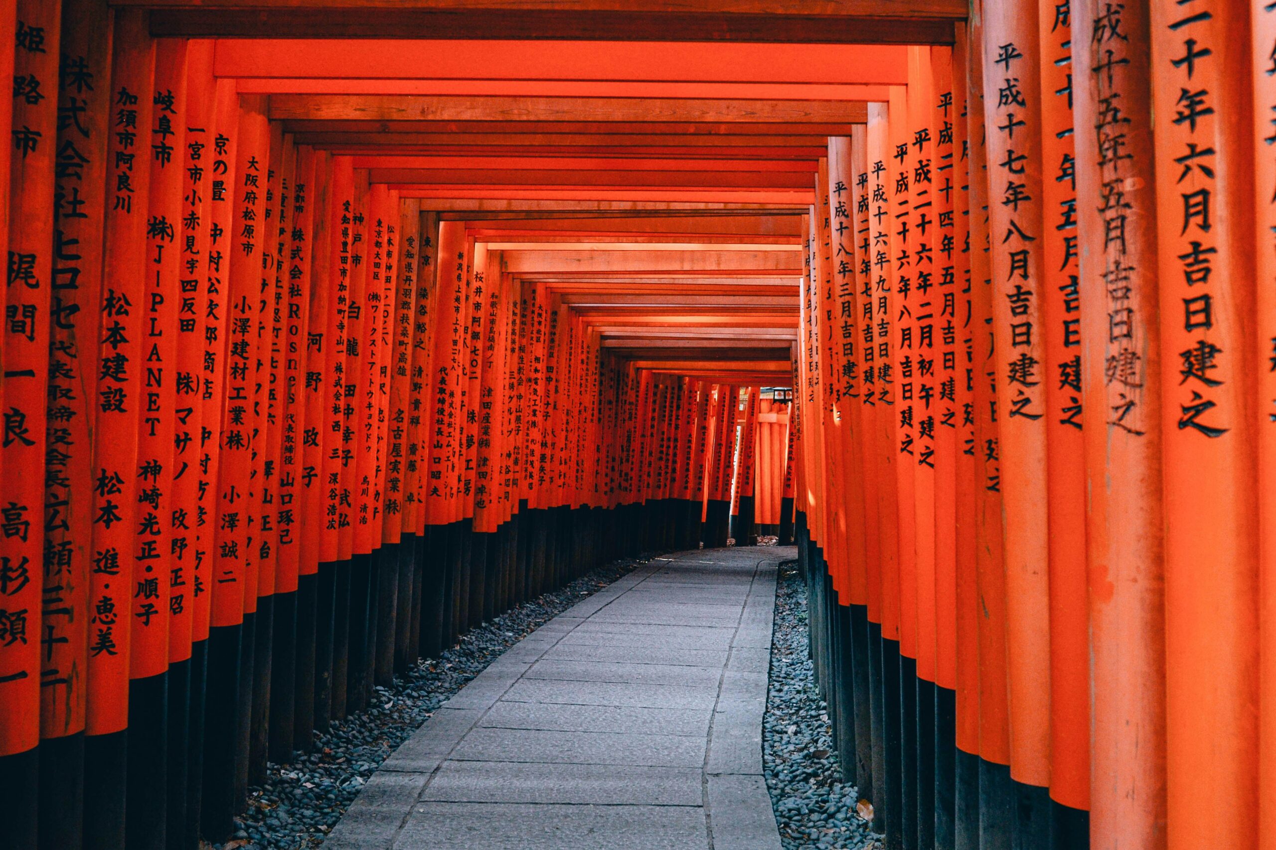 Corredor de portais torii vermelhos com inscrições em japonês no Santuário Fushimi Inari, em Kyoto, Japão