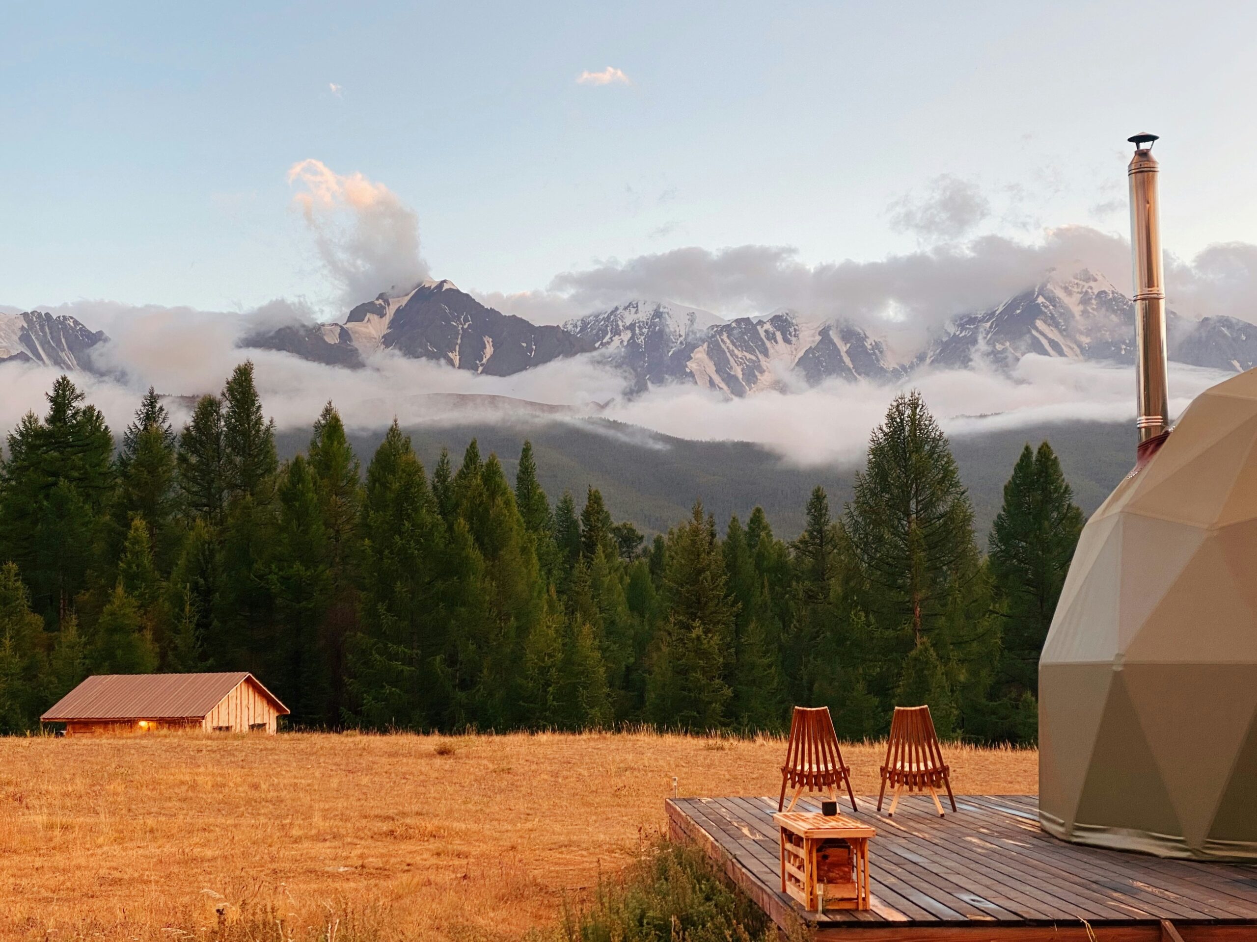 Domo geodésico de glamping de luxo com deck de madeira e vista para cordilheira nevada ao entardecer